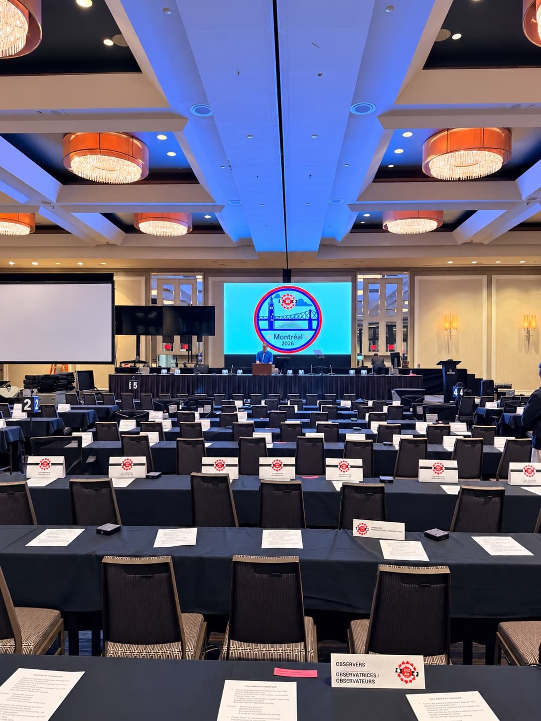 Hotel ballroom set for a conference, with delegate tables facing an LED display at the head table