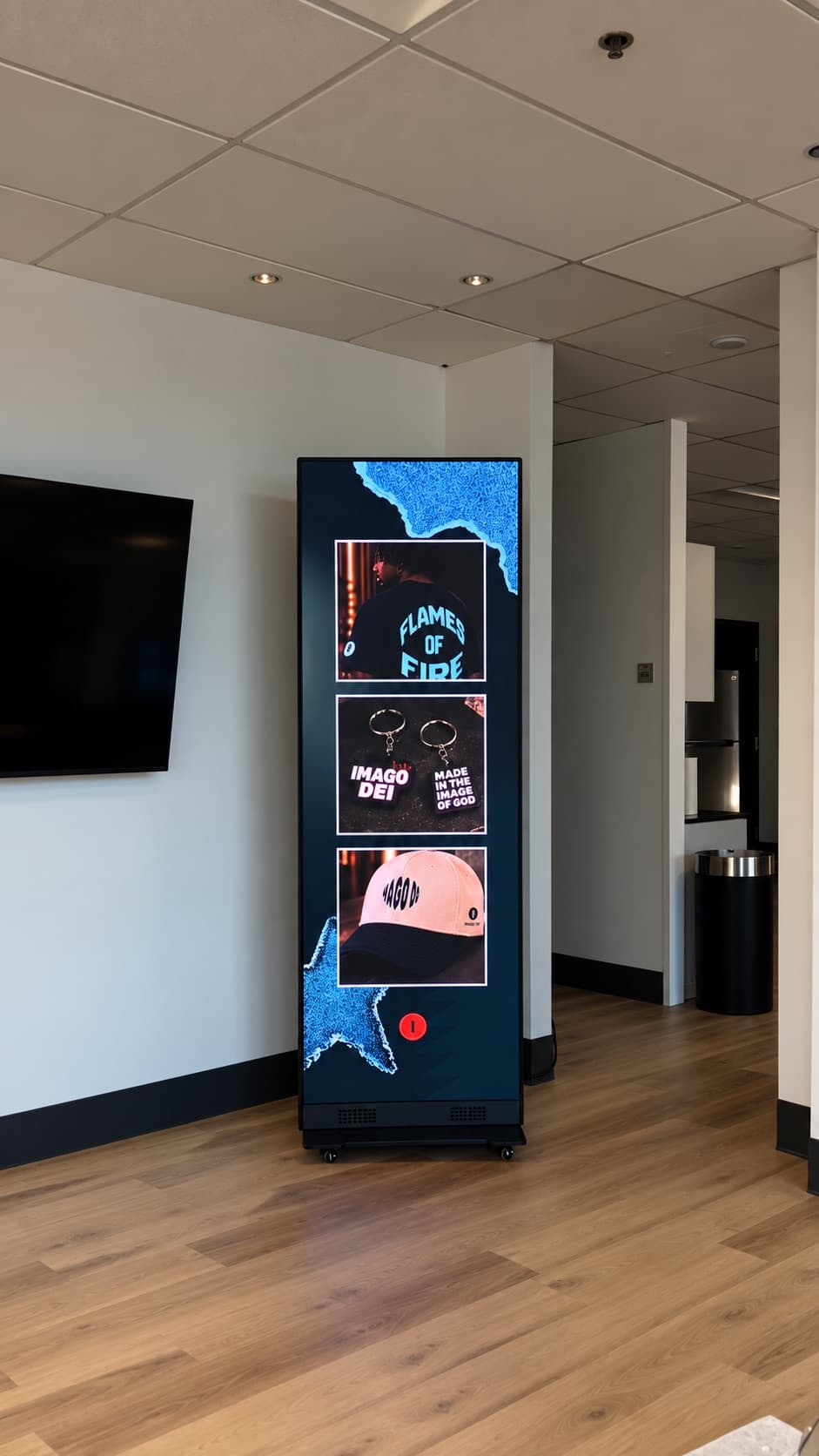 Freestanding portrait LED poster display on wheels showing branded merchandise in a lobby