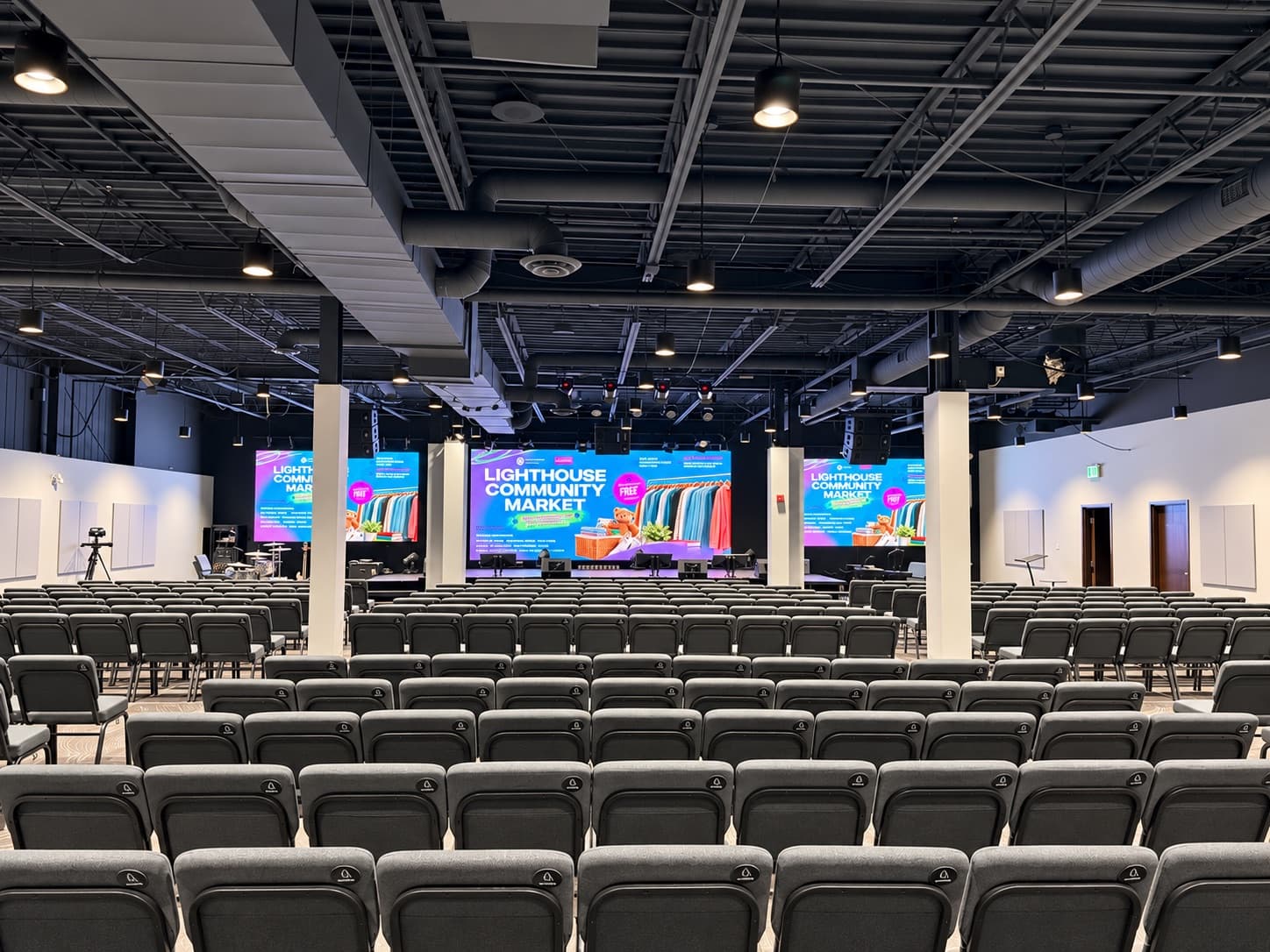 Auditorium with a large centre LED wall and two side LED walls above the stage, facing rows of seating
